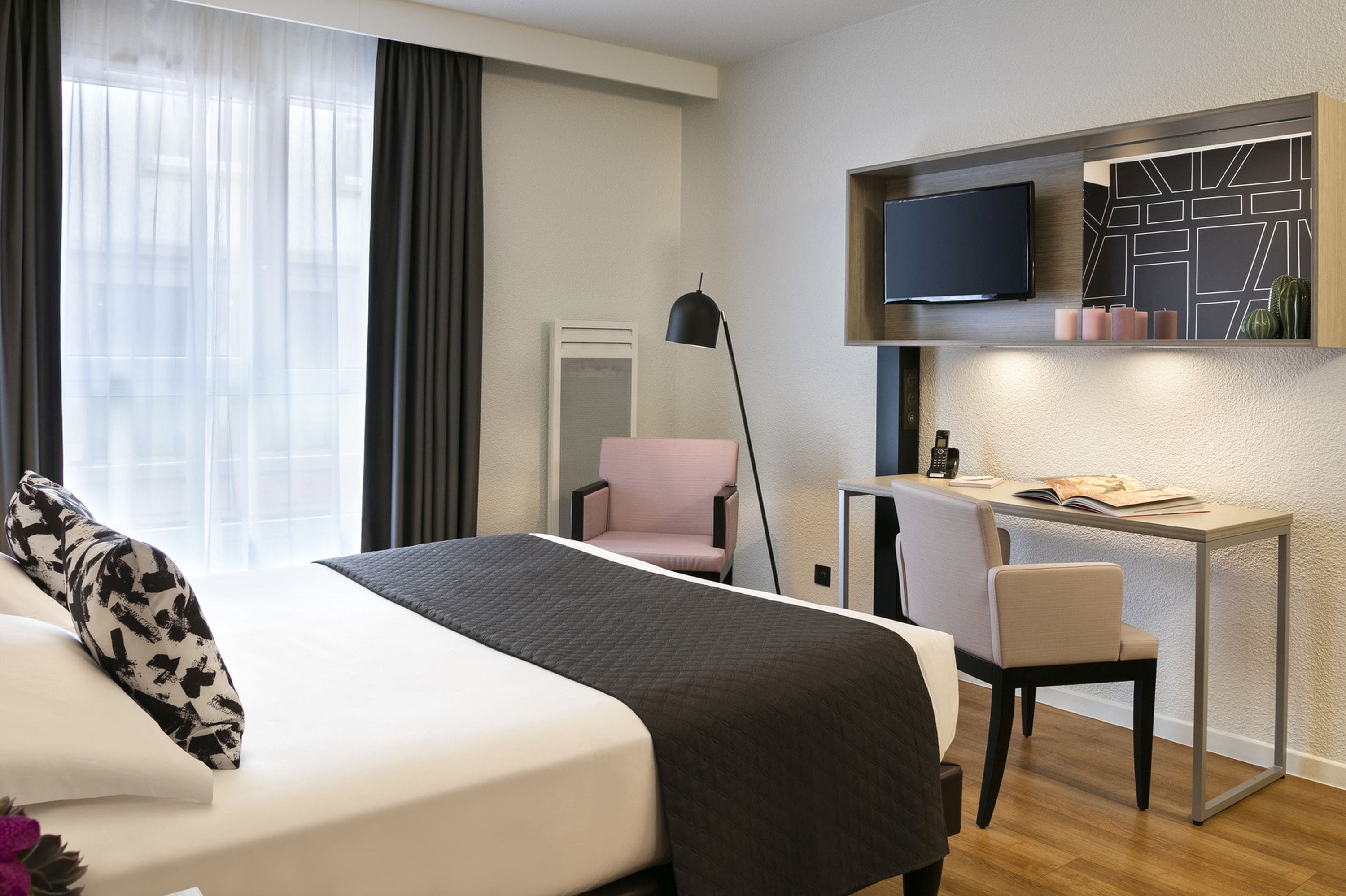 Una habitación de hotel moderna con una cama grande, un escritorio con una silla, un televisor montado en la pared y una ventana con cortinas.