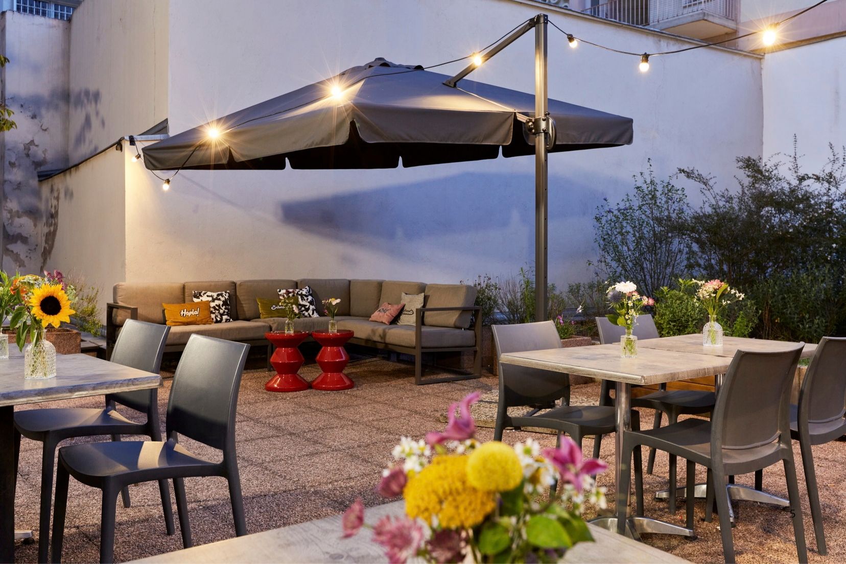 Un espace extérieur aménagé en patio, avec un coin salon couvert, une table à manger avec des chaises et des fleurs décoratives.
