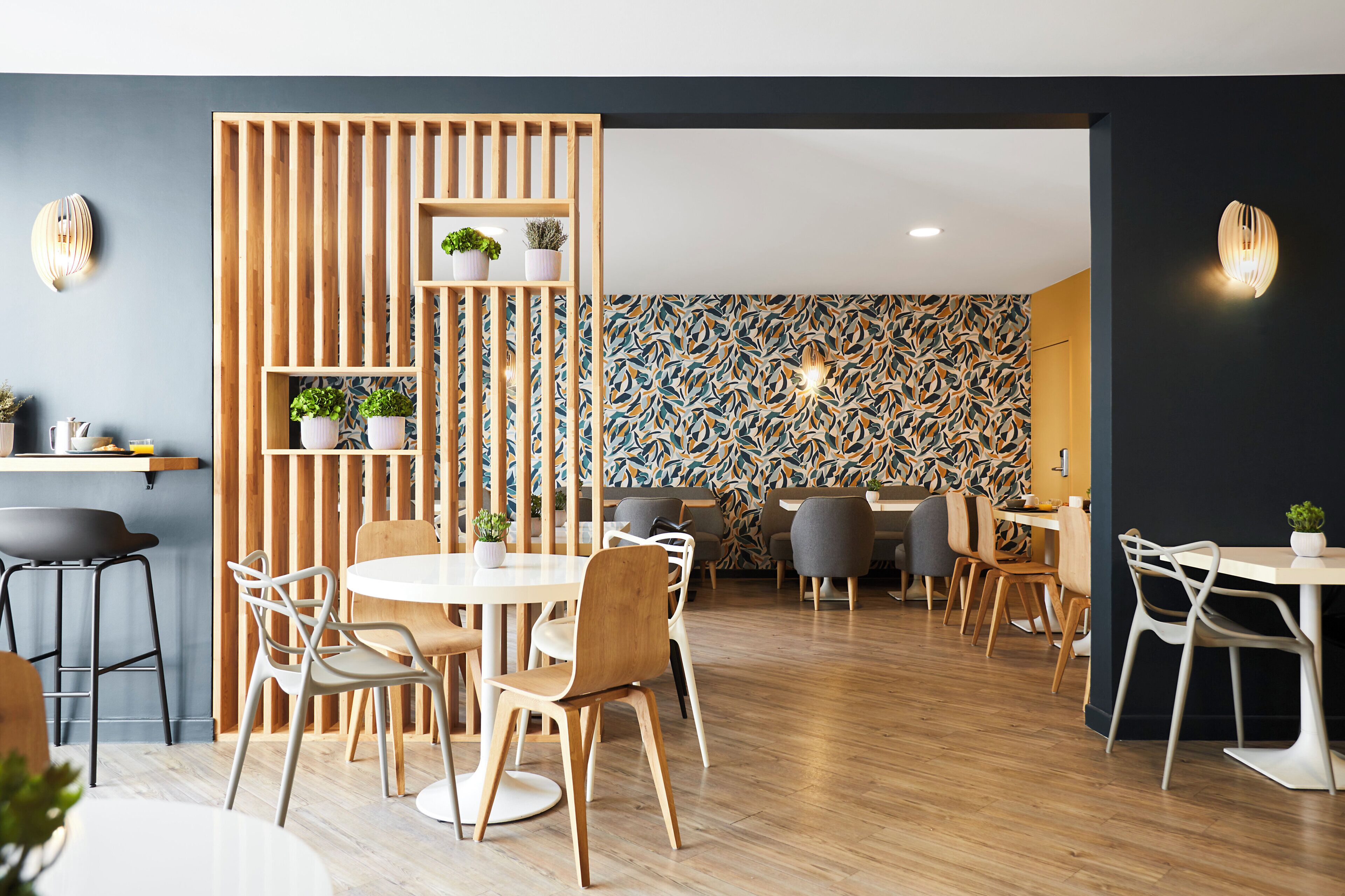 Un espace de restauration moderne avec des cloisons en bois, des tables rondes blanches et des chaises grises.