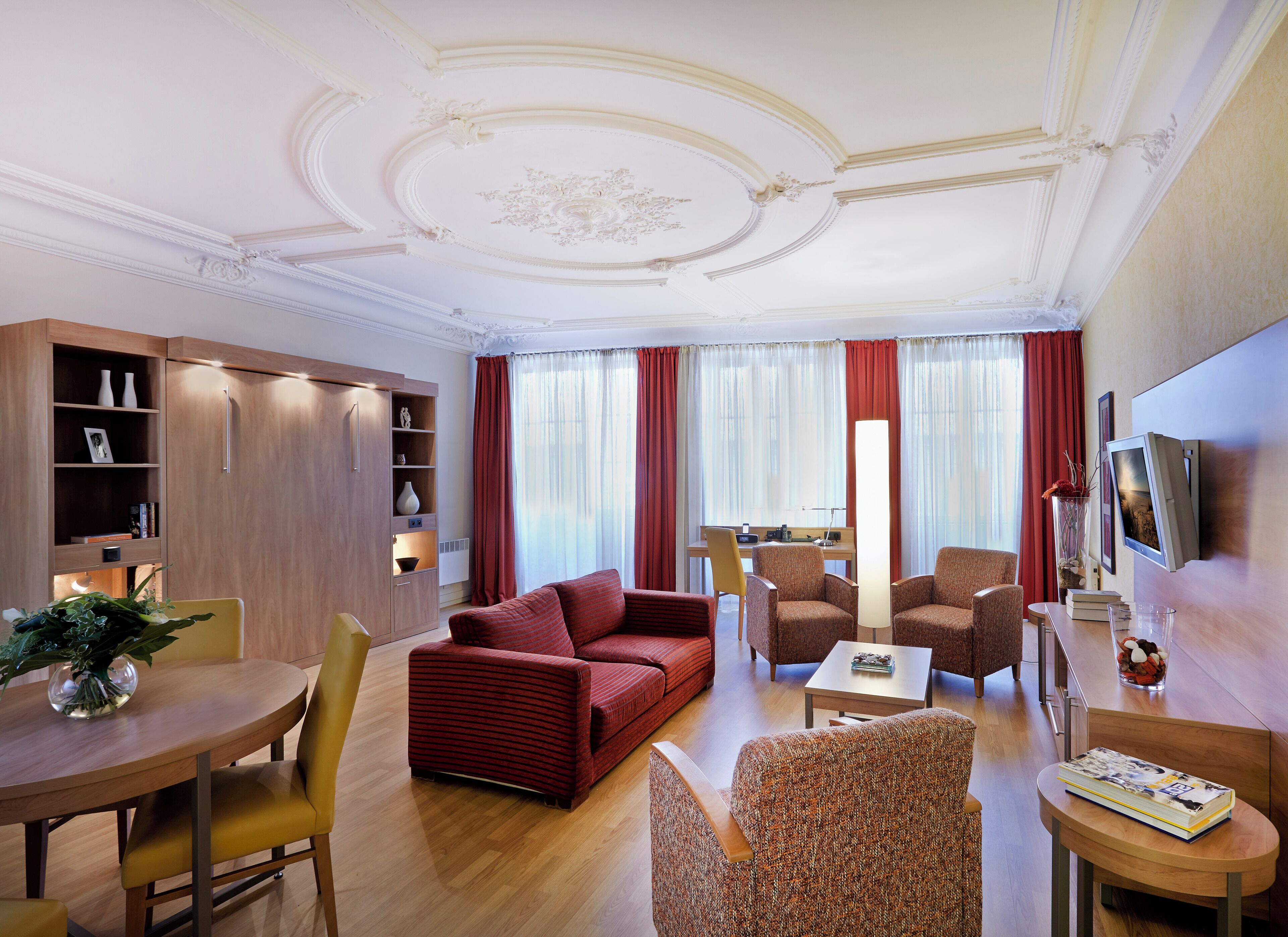 Una habitación de hotel moderna con sofá, sillones, una mesa de comedor y televisión.