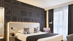 A modern hotel room with a large bed, a bedside table with a lamp, and a view of the city through sheer curtains. - Citadines Kléber Strasbourg (Strasbourg)