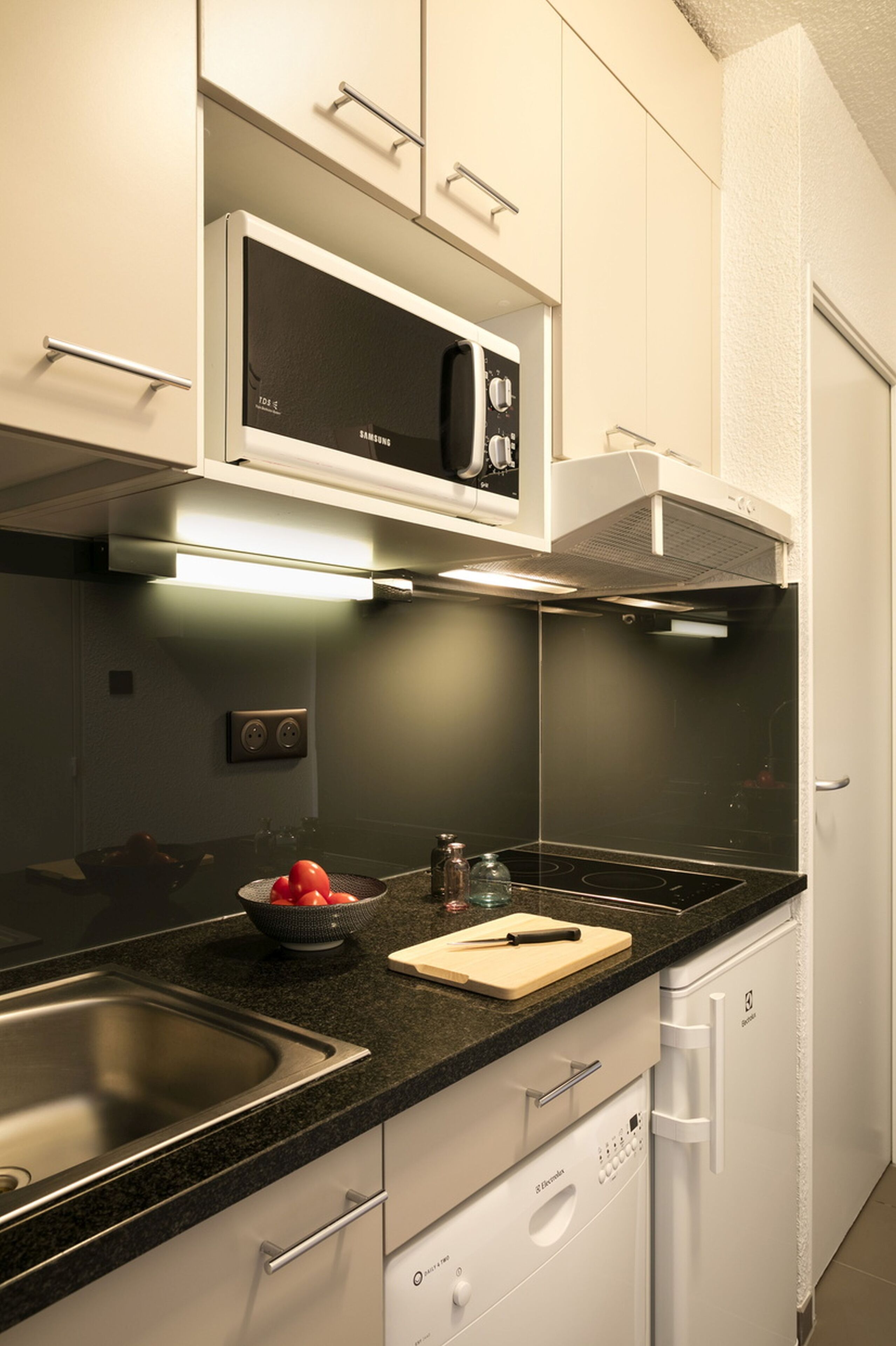 A modern kitchen with a black countertop, stainless steel sink, white cabinets, a microwave, and a dishwasher.