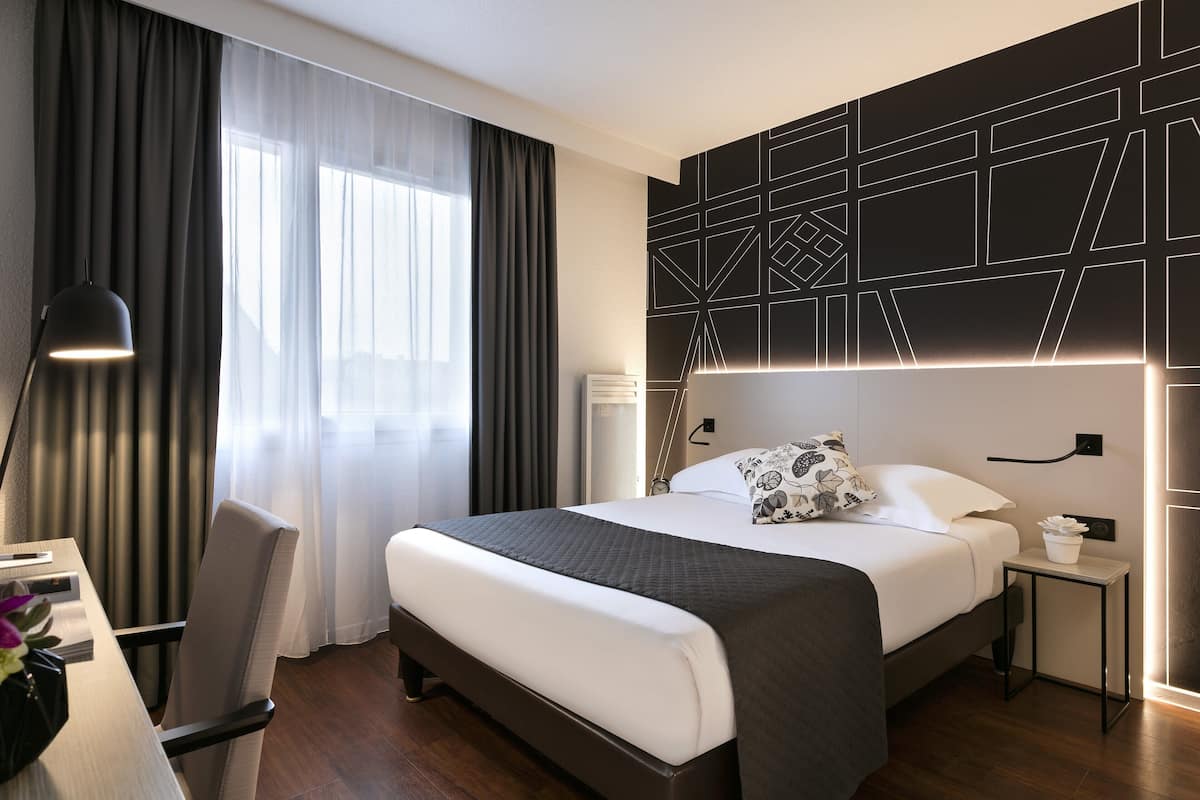 Una habitación de hotel moderna con una cama grande, mesitas de noche, un escritorio y una silla.
