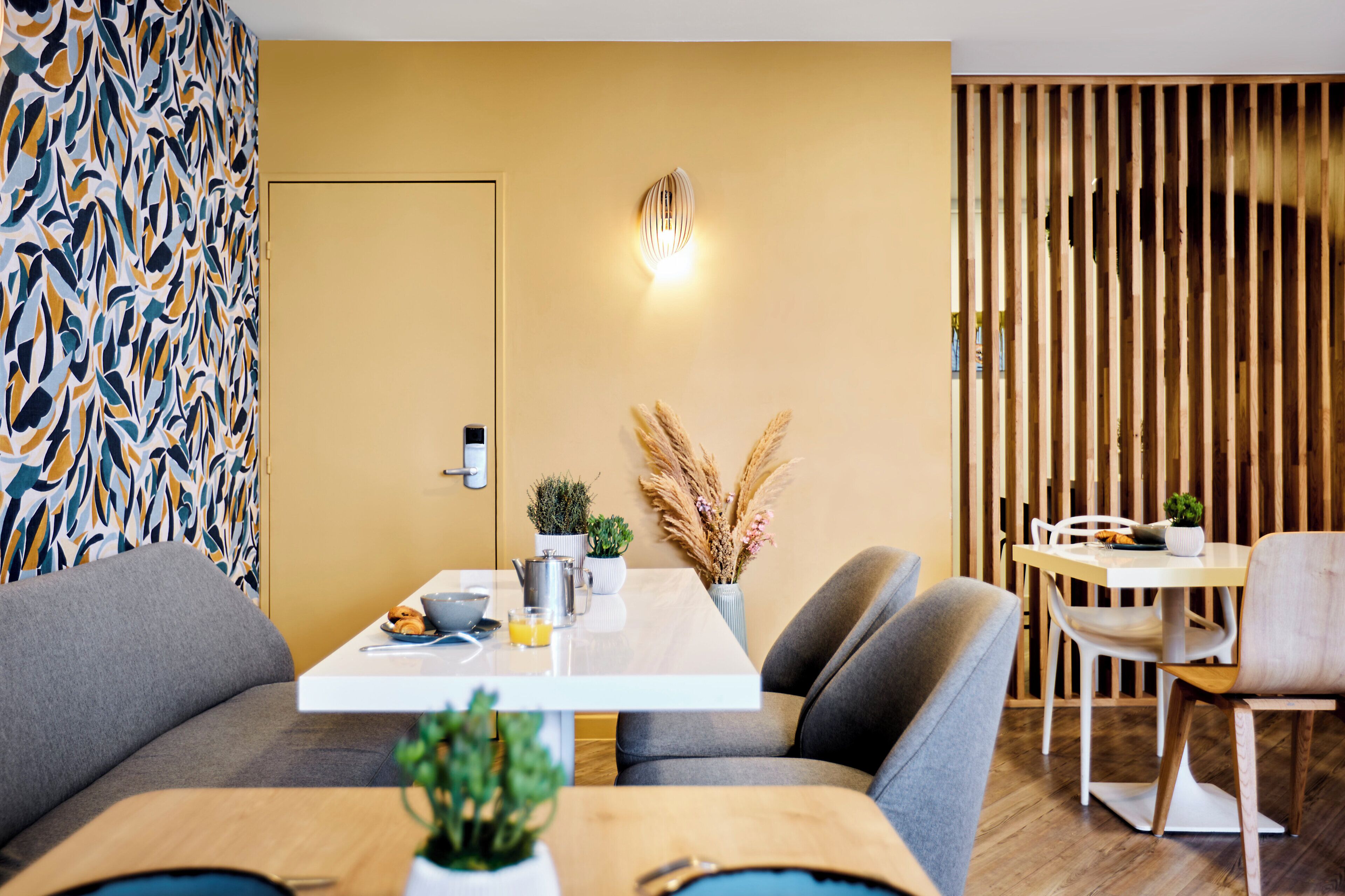 A modern dining area with a white table, grey upholstered chairs, and a wooden partition.