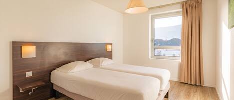 A bedroom with a wooden headboard, two beds, a nightstand, a window with curtains, and a view of the outside.