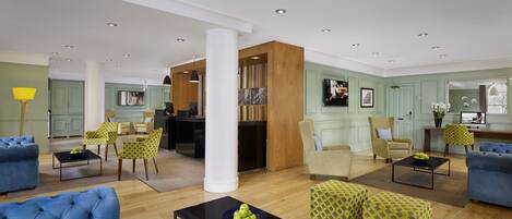 A spacious living area with blue sofas, patterned ottomans, and a black coffee table.