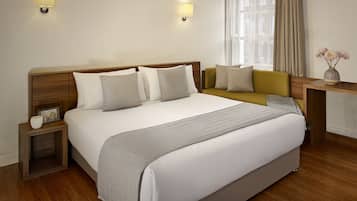 Ett hotellrum med en stor säng, sängbord, en soffa, ett litet bord, en vas med blommor och ett fönster med gardiner.