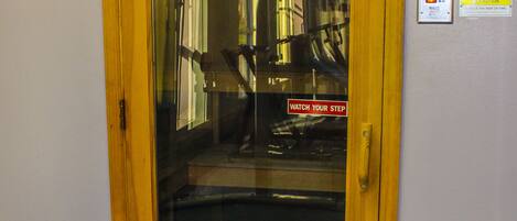 A wooden elevator door with a glass panel, a warning sign, and a caution sign on the wall.