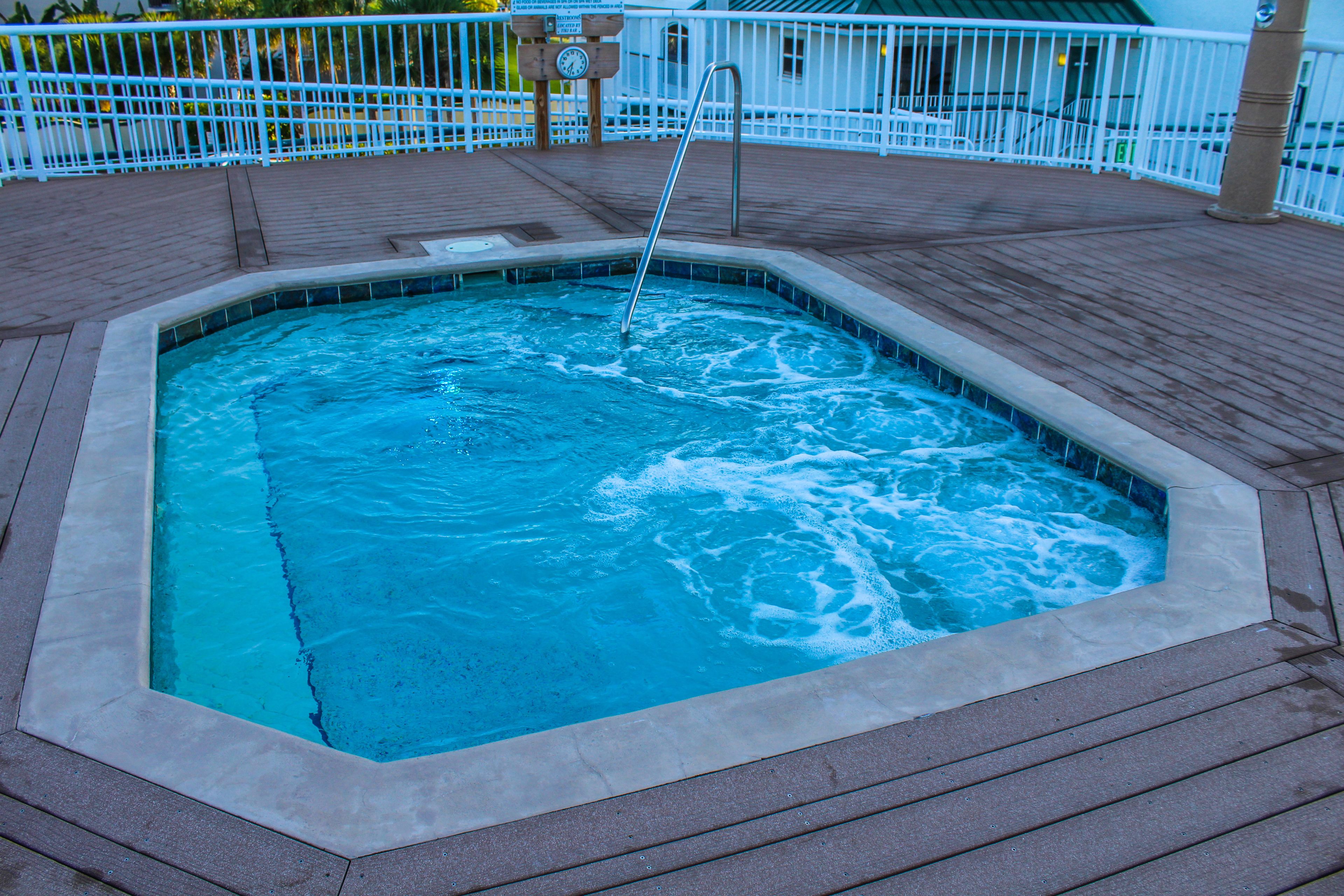 A rectangular hot tub surrounded by a wooden deck with a metal ladder.