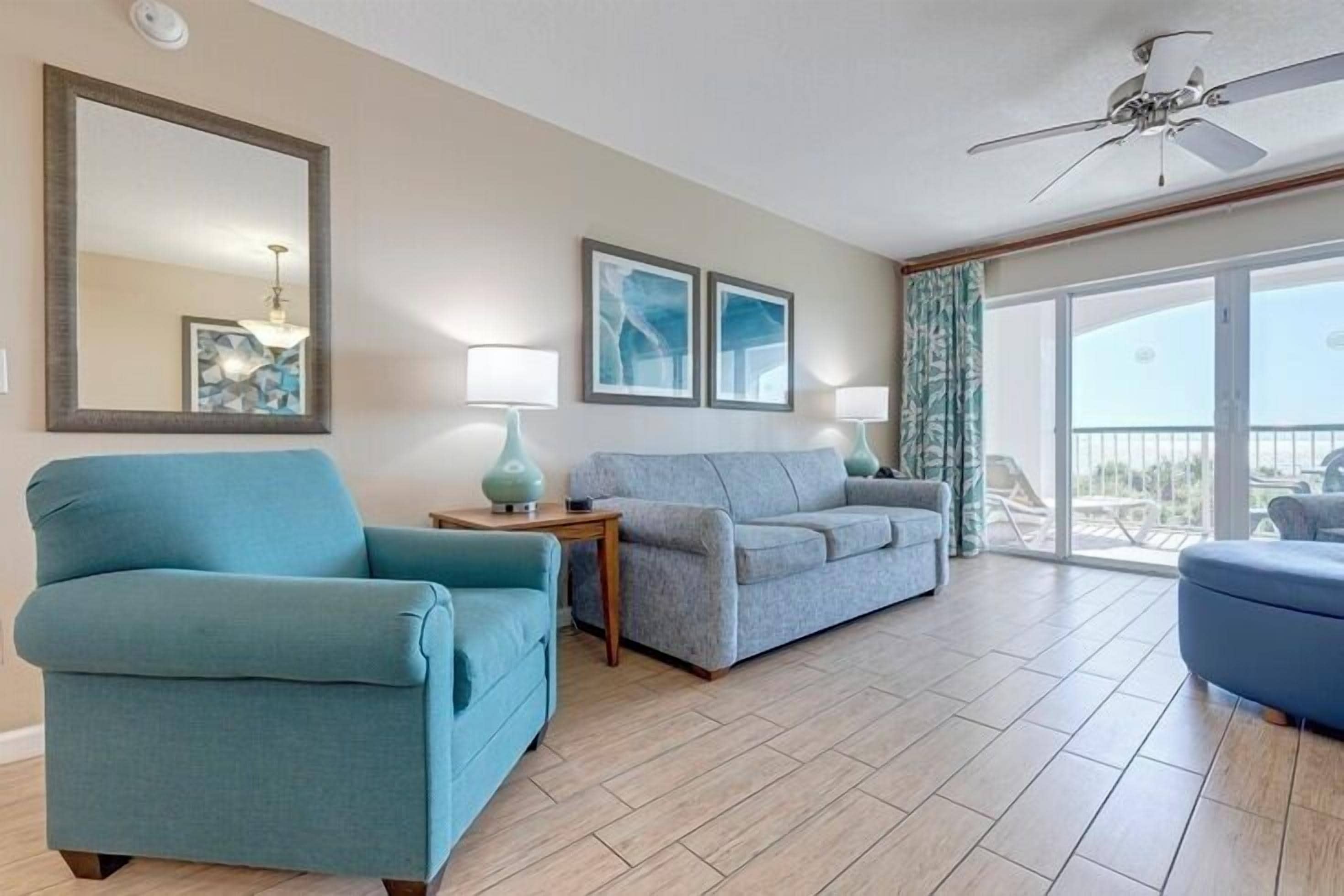 A spacious living room with a blue armchair, a grey sofa, and a balcony with a view.