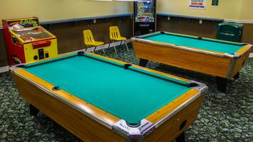 Deux tables de billard dans une pièce dont le sol est recouvert d’une moquette verte, avec des chaises jaunes, et une autre table de billard à l’arrière-plan.