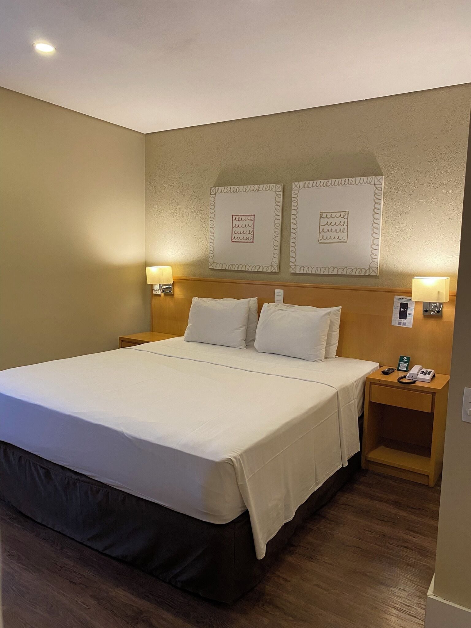 A hotel room with a large bed, two bedside tables, and wall-mounted artwork.
