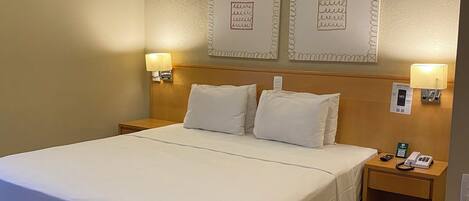 A hotel room with a large bed, two bedside tables, and wall-mounted artwork.