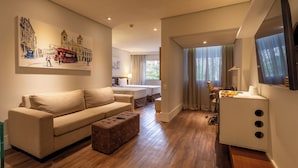 Una habitación de hotel moderna con sofá, reposapiés y zona de comedor con mesa y sillas.