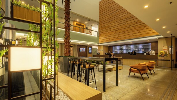 Un moderno vestíbulo de hotel con mostrador de recepción, área de descanso y una gran exhibición de plantas.