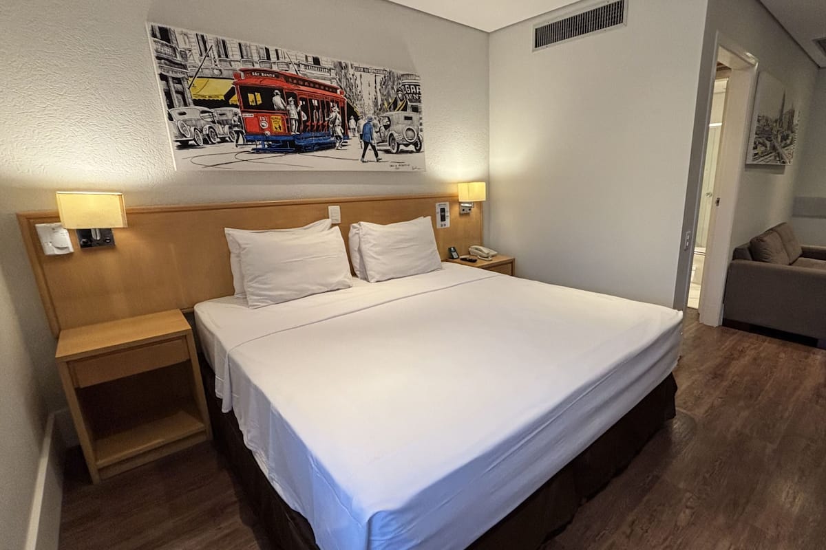 A hotel room with a large bed, bedside tables, a nightstand, a chair, and a wall-mounted artwork.