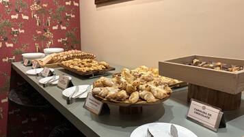A buffet with various pastries and bread, including a sign for 'Polvado de Maçã Apple Pudding Pastry.'