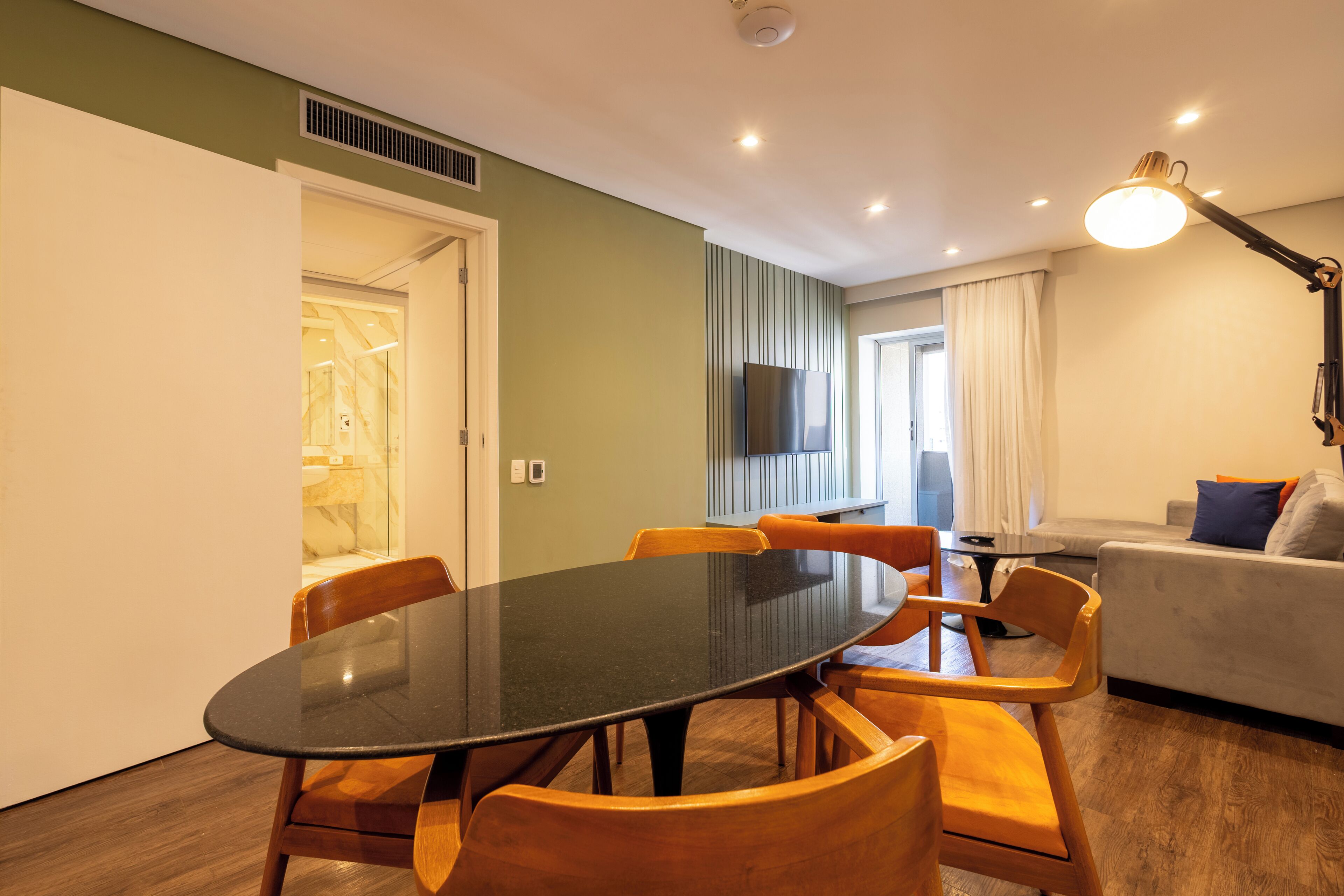 Een moderne woonkamer met een eettafel, houten stoelen, een bank en een aan de muur bevestigde televisie.