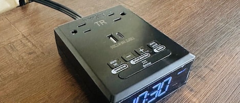 Una regleta de enchufes negra con un reloj digital que marca las 12:30, conectada a un tomacorriente.