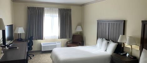 Une chambre d’hôtel avec deux lits, un bureau avec un ordinateur et une lampe, une chaise, un téléviseur et une fenêtre avec des rideaux.