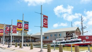 Un muelle con varios letreros que indican 'Pier 21', un edificio grande con techo plano y un barco histórico amarrado cerca.