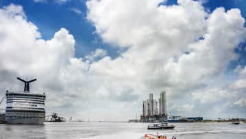 Un crucero llamado "Carnival Triumph" atracado en un puerto, con un bote a motor en primer plano y edificios industriales al fondo.