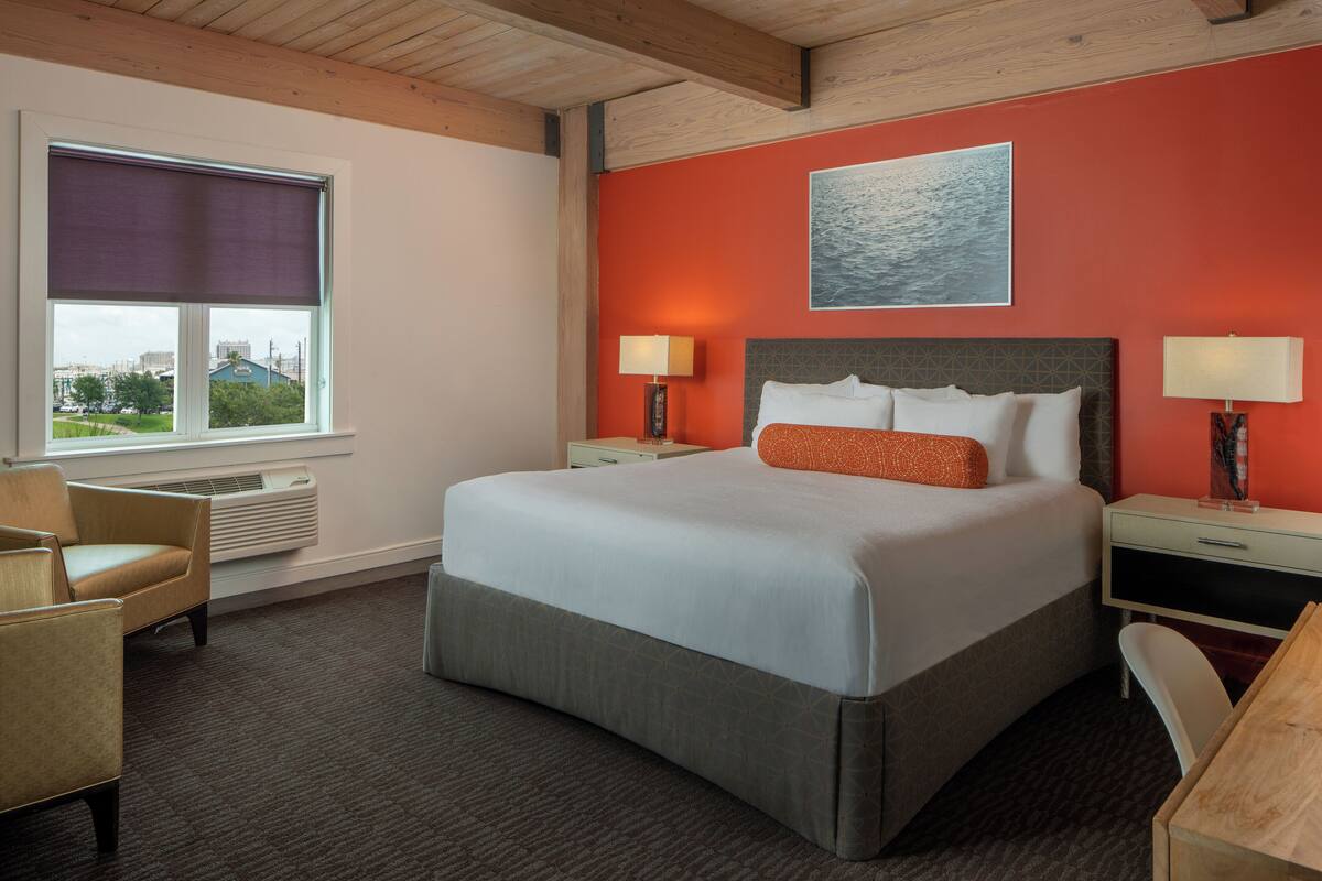 A hotel room with a large bed, two bedside tables with lamps, a chair, a desk, and a window with a view of the city.