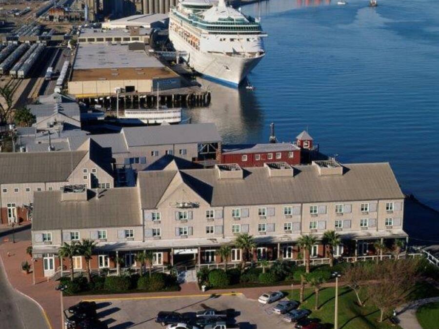A large hotel with a parking lot and a cruise ship docked nearby.