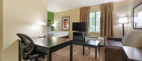 A hotel room with a desk, office chair, television, sofa, and a small table.