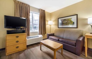 A furnished room with a flat-screen TV, a sofa, a wooden table, a lamp, and a framed picture on the wall.