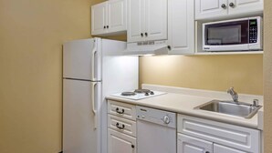 Une cuisine compacte avec des meubles blancs, un four à micro-ondes encastré, un réfrigérateur, une cuisinière et un évier.