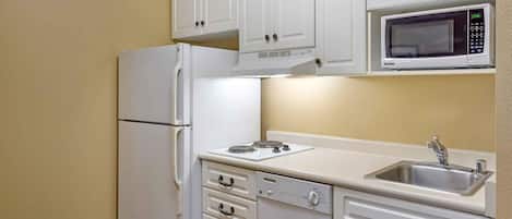 Cocina compacta con muebles blancos, microondas integrado, refrigerador, estufa y lavaplatos.