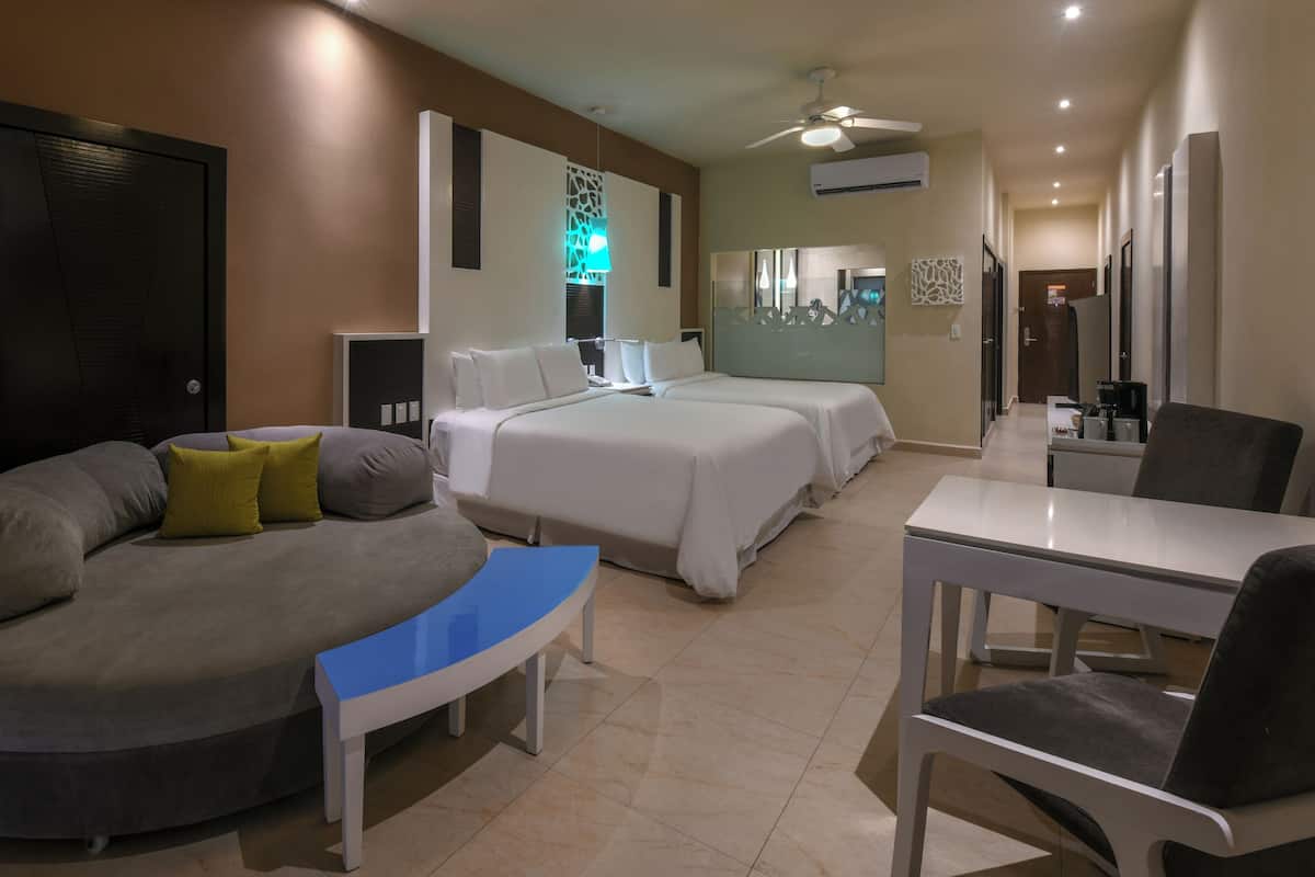 Una habitación de hotel con un sofá curvo, dos camas, un escritorio y una silla.
