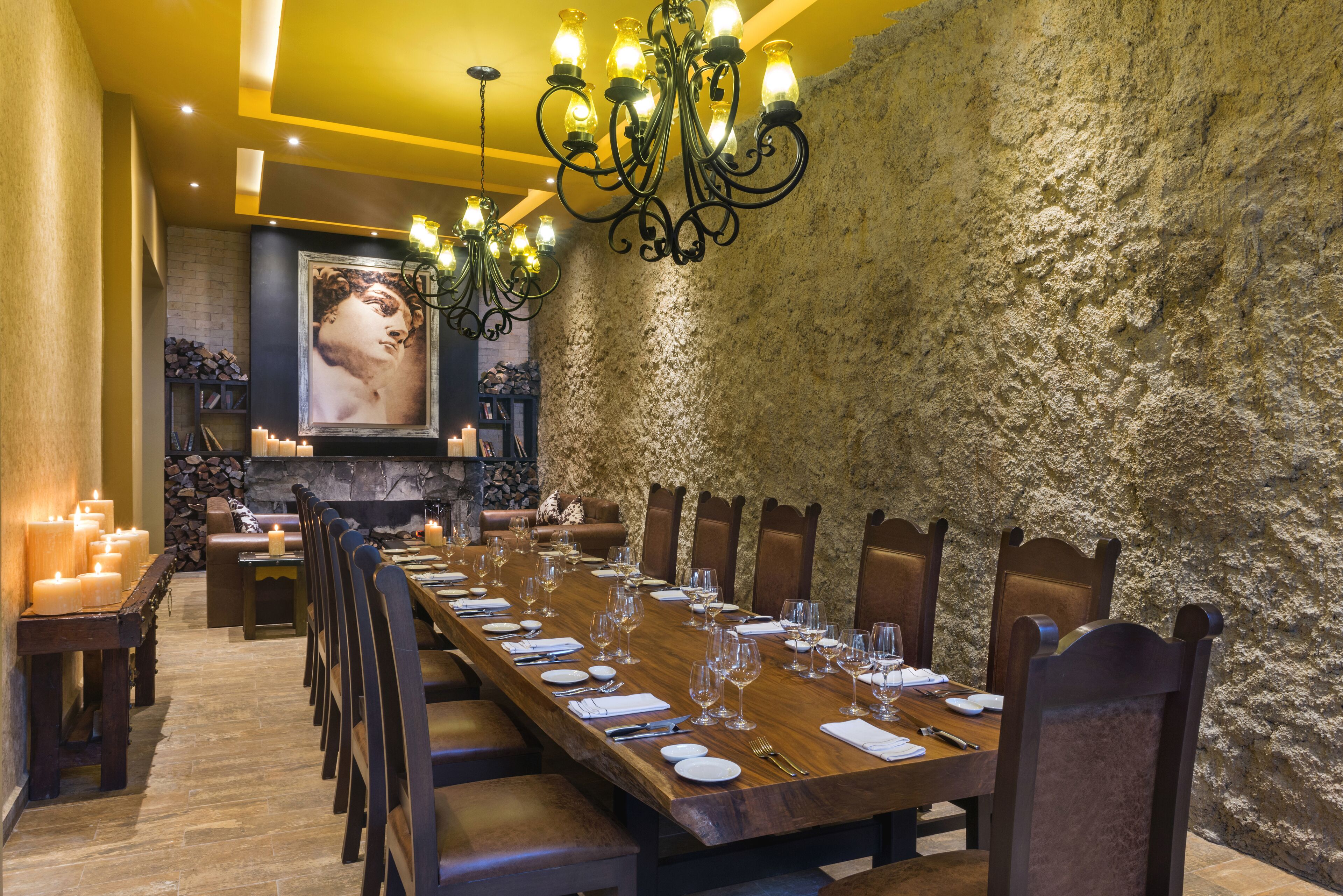 Un comedor formal con una larga mesa de madera dispuesta para una comida, rodeada de sillas y una gran araña colgante.