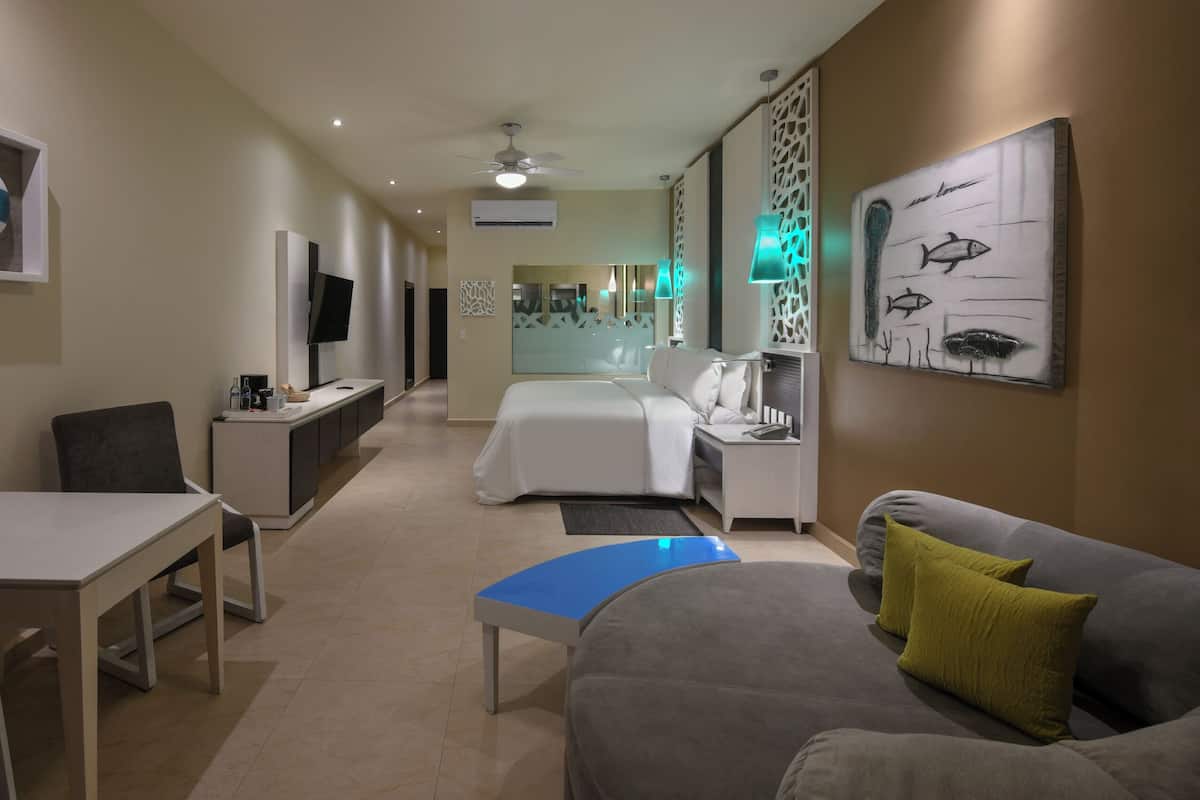 Habitación de hotel con cama, sofá, escritorio, televisor y obras de arte en las paredes.