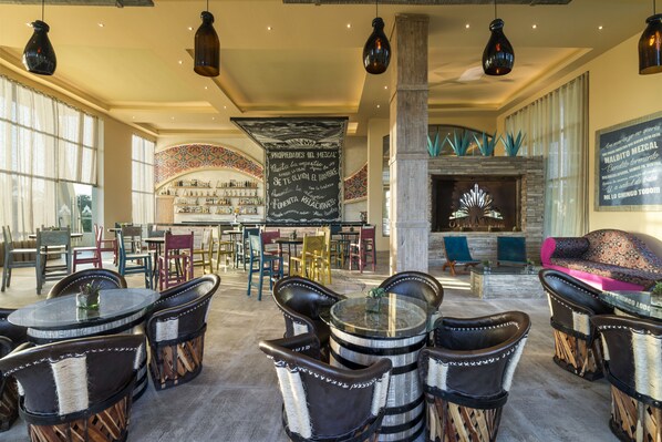 A spacious lobby with round tables and chairs, a fireplace, and a bar area with shelves of bottles.