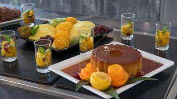 Un plato de postres con varias frutas y un flan de caramelo sobre una bandeja.