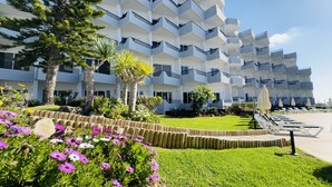 Un hotel moderno con una estructura de varios pisos, un césped cuidado y una zona de piscina con tumbonas.