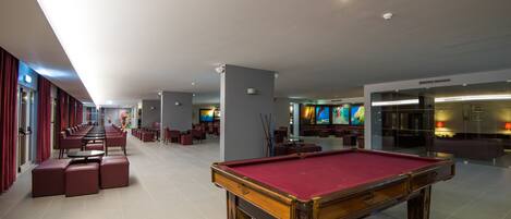 A spacious indoor area with a pool table, seating areas, and a long corridor with red curtains.