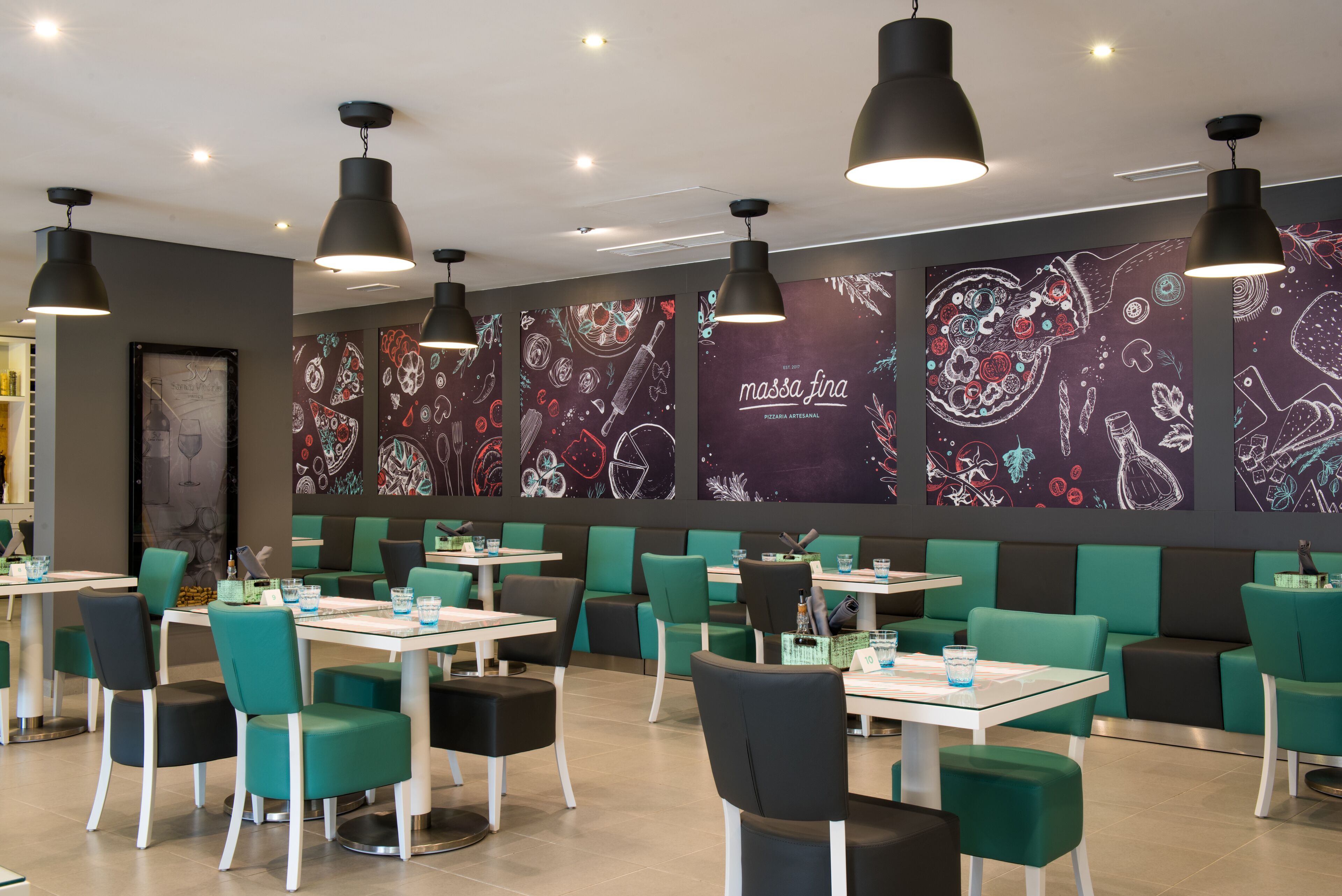 Een restaurant met smaragdgroene en zwarte stoelen, witte tafels en zwarte hanglampen.
