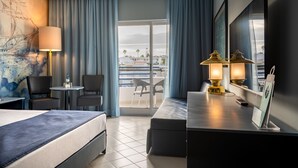 Habitación de hotel con cama, dos sillas, una mesita, lámpara, televisor y balcón con vistas a la ciudad.
