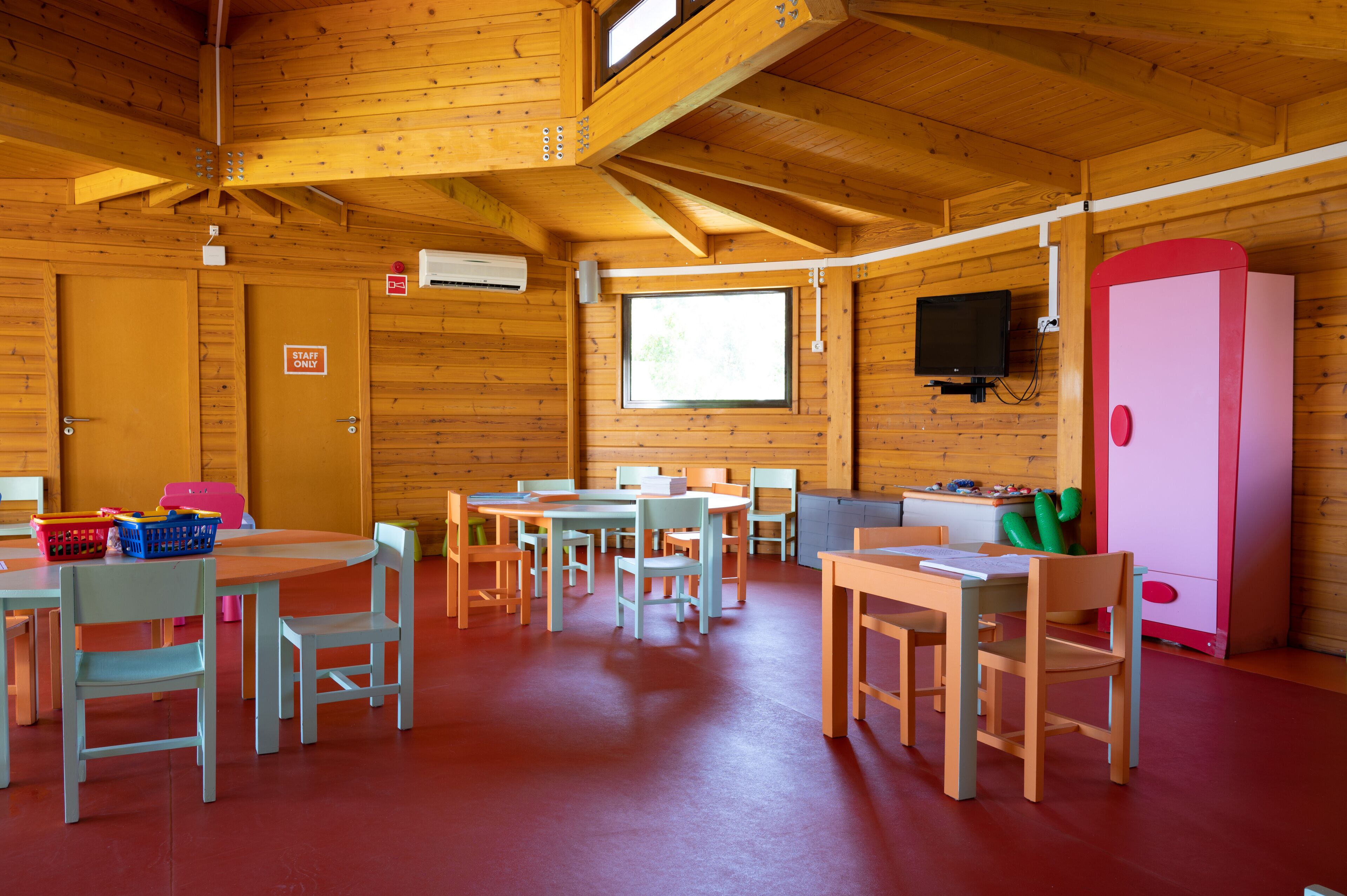 A wooden cabin with multiple tables and chairs, a television, and a pink cabinet.