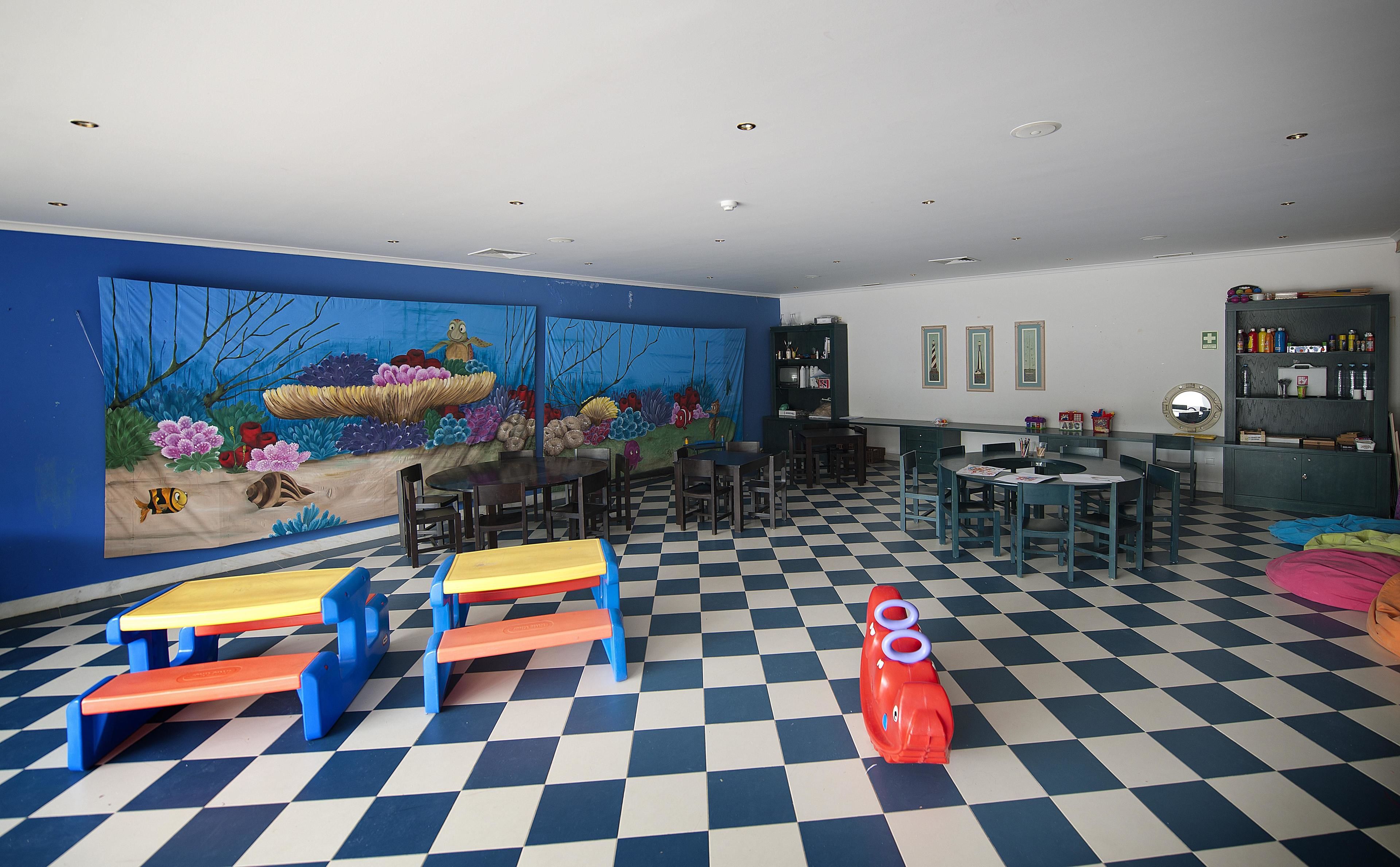 A room with a blue and white checkered floor, a mural of an underwater scene on the wall, and a bookshelf filled with books and items.