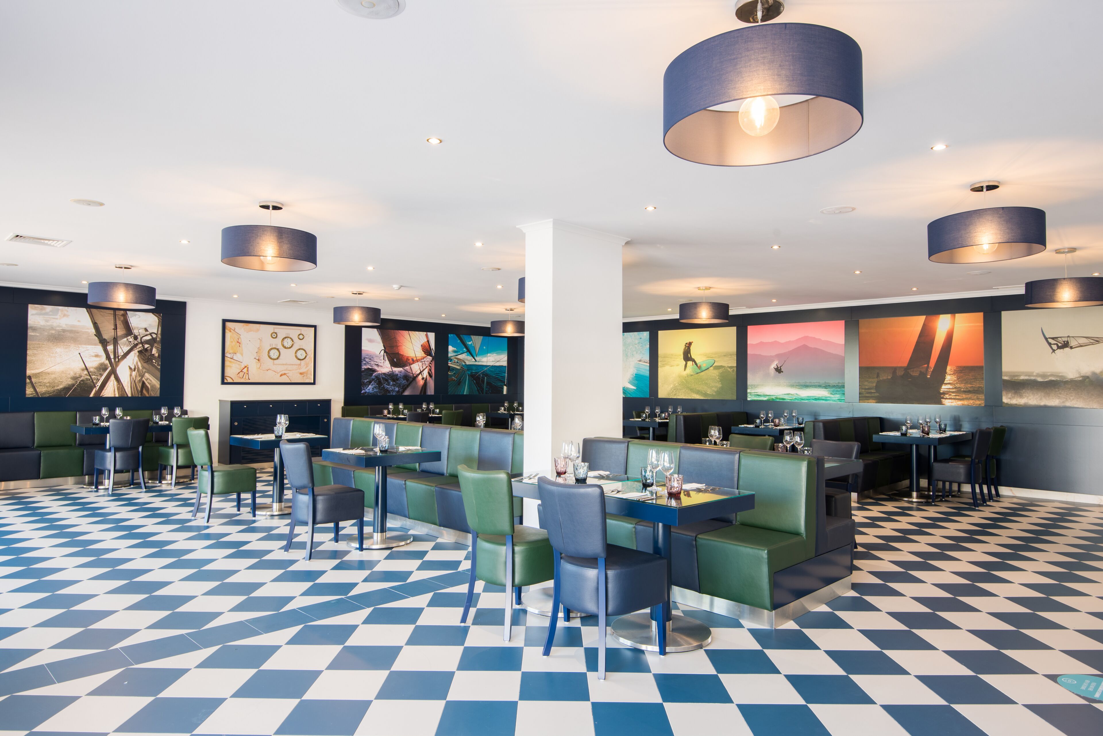 En modern restaurang med rutmönstrat golv, gröna bås och blå hänglampor.