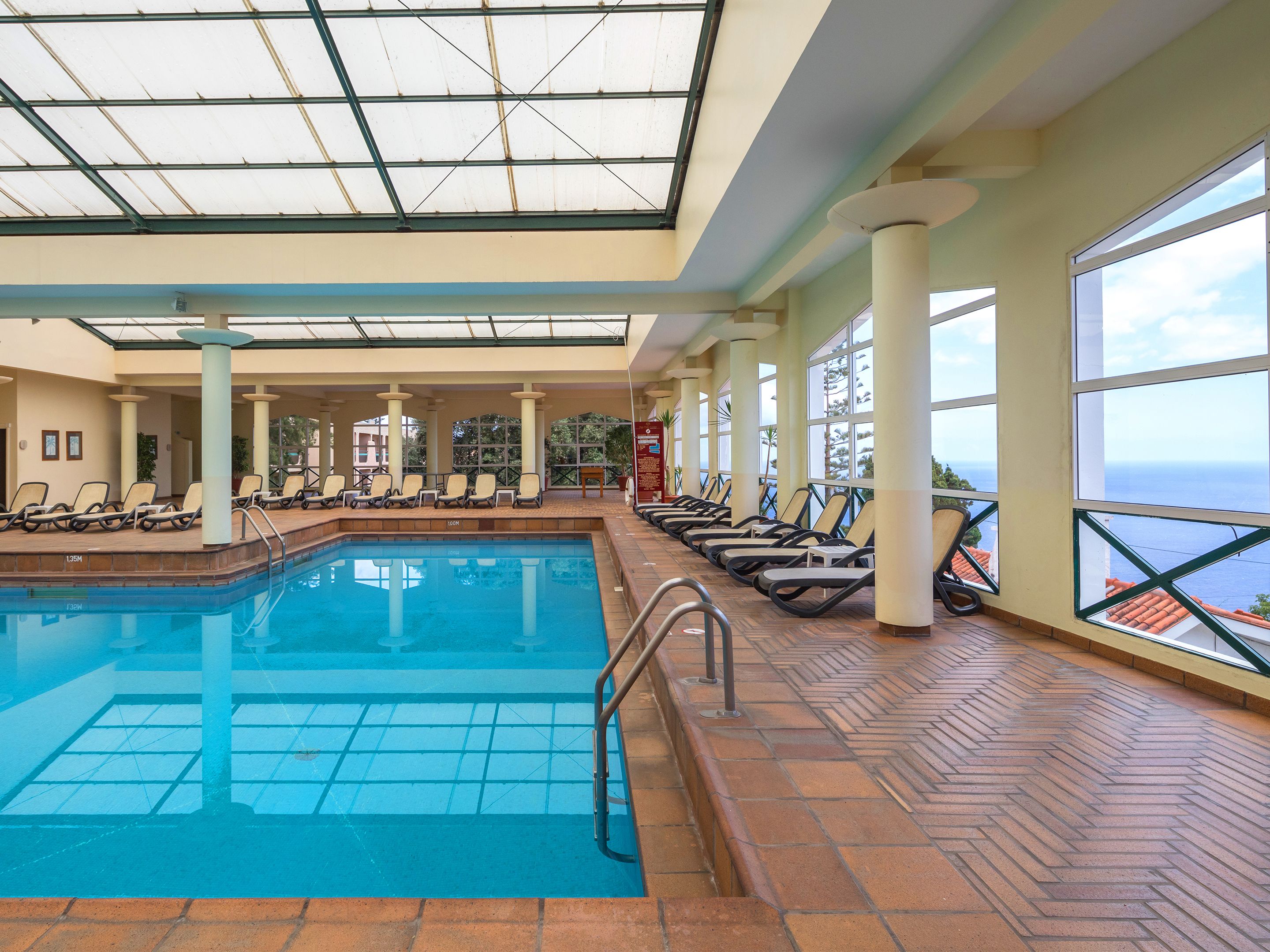 An indoor swimming pool with lounge chairs and a view of the ocean.