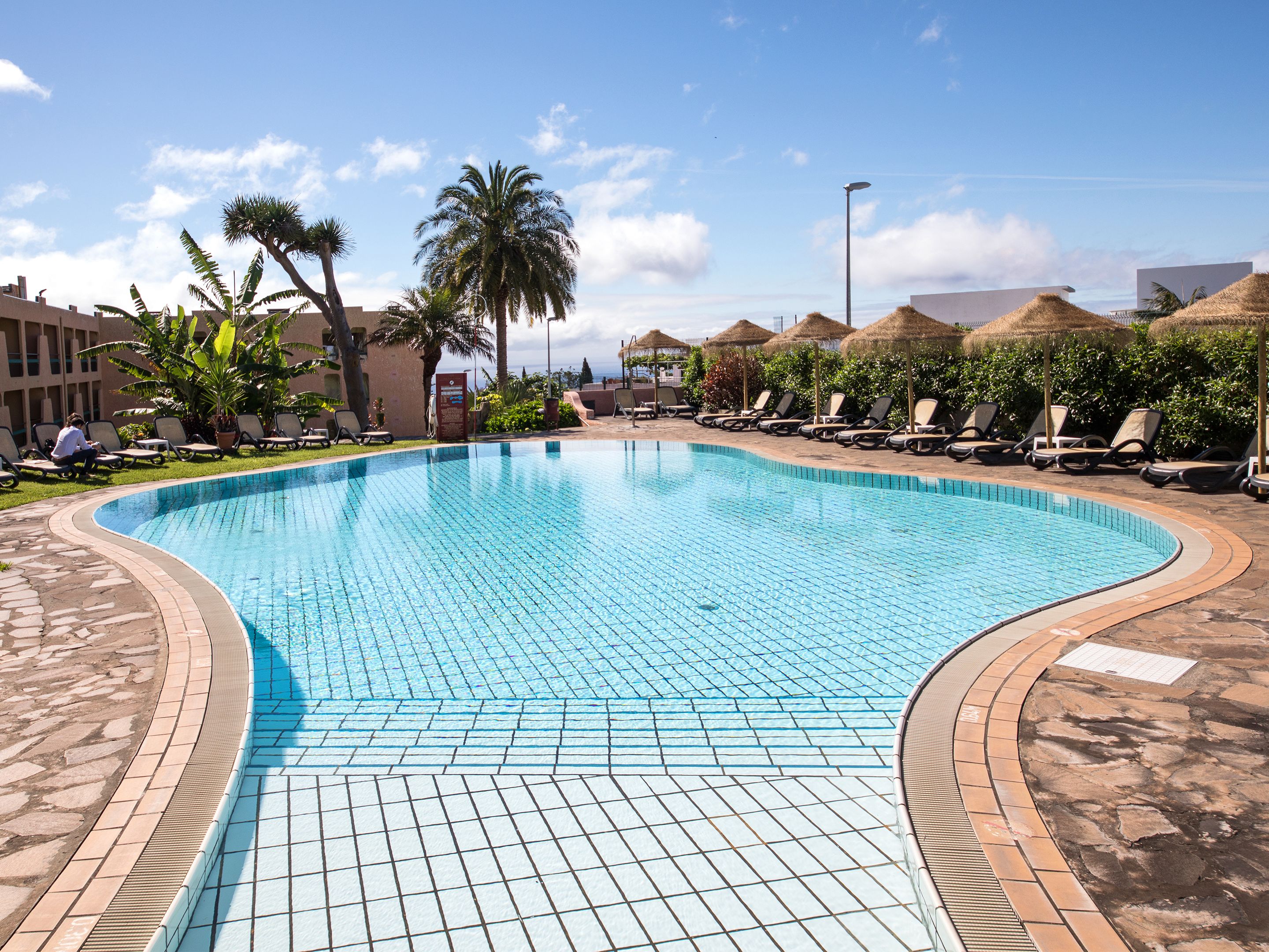Una piscina con bordes de azulejos, rodeada de sillas de descanso y palmeras.