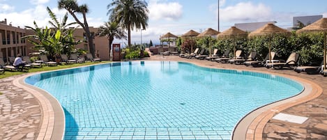 Una piscina con bordes de azulejos, rodeada de sillas de descanso y palmeras.