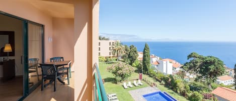 Un balcón con mesa y sillas, una piscina y vista al mar.