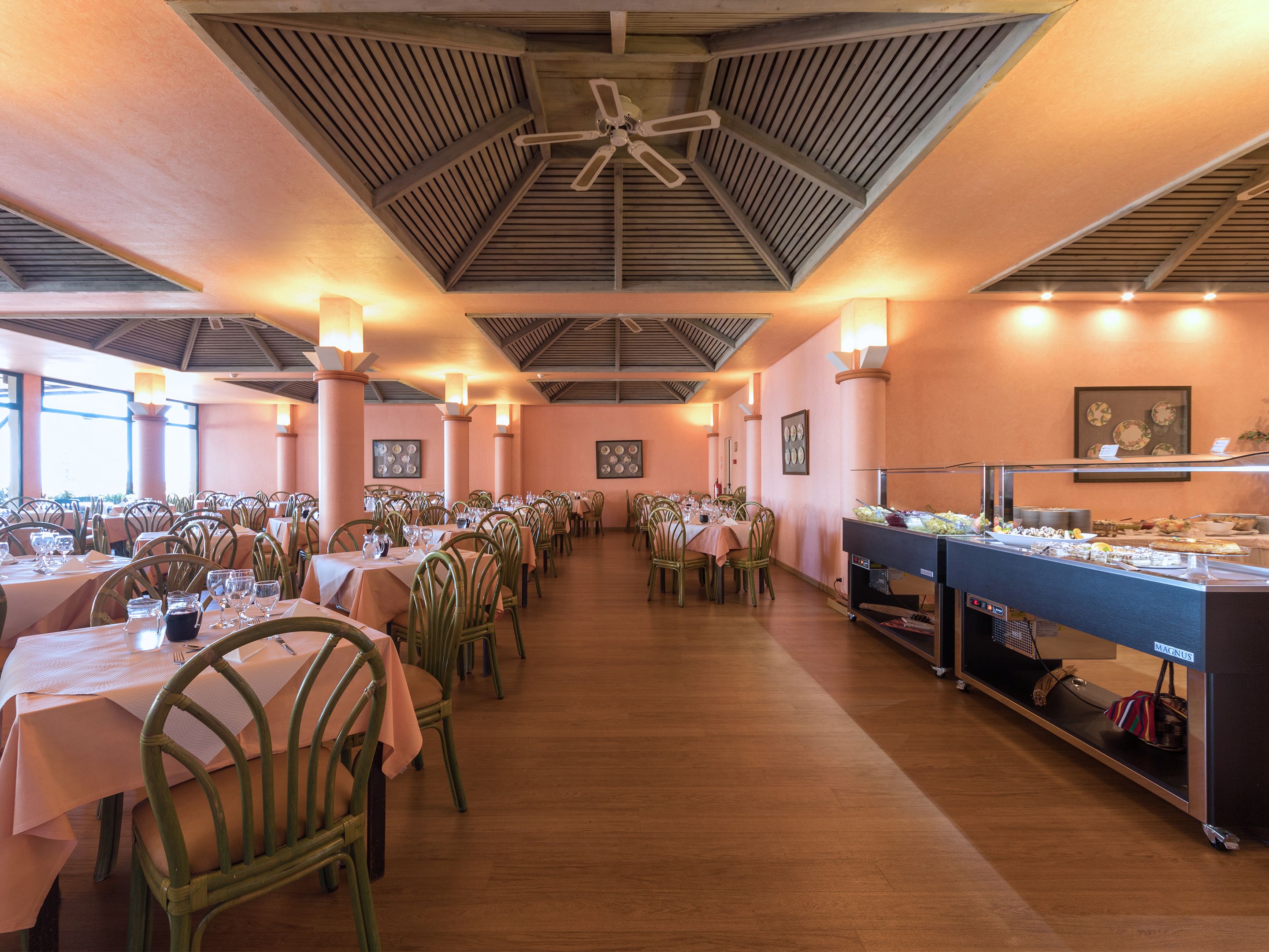 Un comedor amplio con varias mesas y sillas, una barra de buffet y un ventilador de techo.