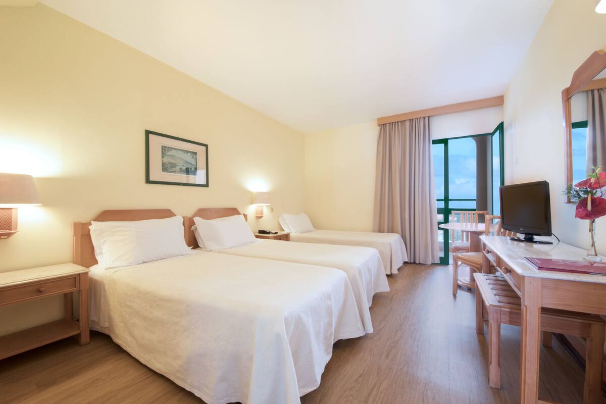 A hotel room with two beds, a desk, a TV, and a window with curtains.